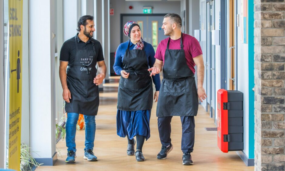 Two men and a woman walking down a hallway wearing Samo'r Cafe aprons