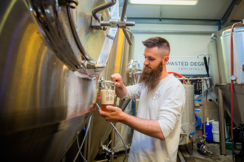 A man with a large beard taps beer out of a big tank.