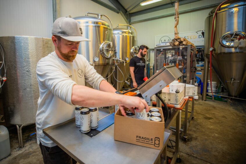 A man putting cans of beer into a cardboard box inside a brewing room.