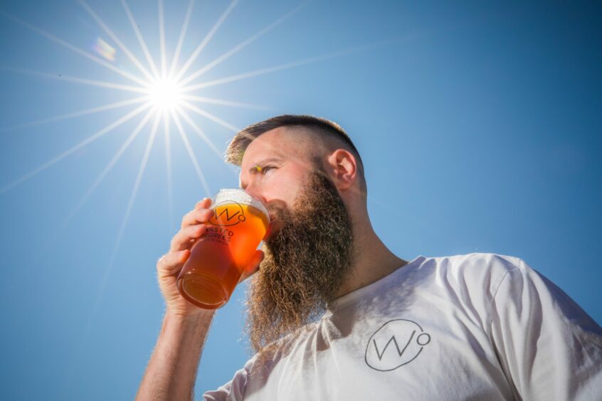 A man drinking a pint of beer outside in bright sunshine.