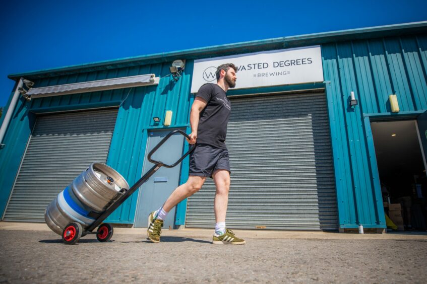 A man dragging a tank of beer behind him outside Wasted Degrees Brewing.