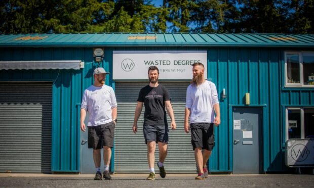 Three men walking outside a blue industrial unit housing Wasted Degrees Brewing.