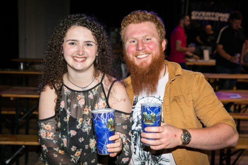 A woman and a man smiling at the camera holding a beer each.
