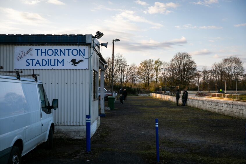 Exterior shot of Thornton greyhound racing stadium in Fife. Picture shows a metal cabin next to a track with a small group of spectators standing by.