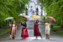 Women standing in street holding parasols.