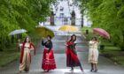 Women standing in street holding parasols.