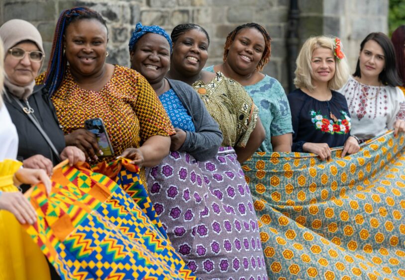 Women in a row with beautiful fabric smiling at the camera.