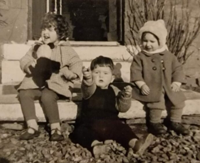 Black and white photo of three small children in 1960s clothing.