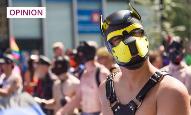 Man on Pride march wearing leather dog mask and bondage gear.