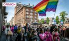 Large crowd of people walking behind a rainbow flag in front of The Courier building in Dundee city centre during the Dundee Pride event.