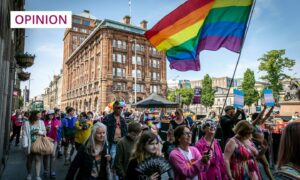 Large crowd of people walking behind a rainbow flag in front of The Courier building in Dundee city centre during the Dundee Pride event.