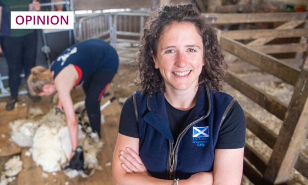 Rural Affairs Secretary Mairi Gougeon in a navy Scottish Government gilet, standing in front of a woman shearing a sheep.