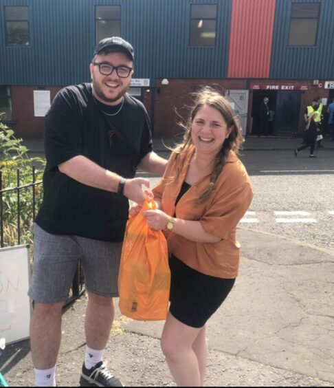 Marty Smith with Mercedes Villalba MSP holding a bag of food donations outside football stadium. Image: Fans Supporting Foodbanks Dundee.