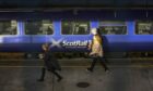 Passengers walking along a platform past a ScotRail train