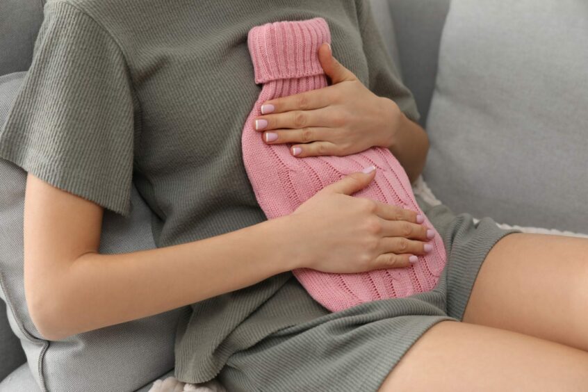 woman holding hot water bottle to abdomen.