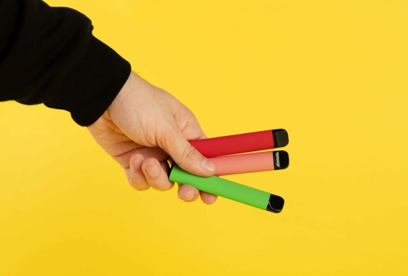hand holding three brightly coloured disposable vapes.