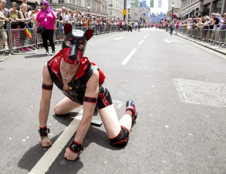 Man in leather shorts and vest and dog mask kneeling down in the street at London Pride in previous years. 