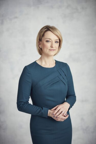 Studio portrait of BBC journalist Laura Kuenssberg in blue dress against a grey background.