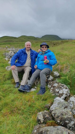 Fred and Maureen Cotterell sitting on a low stone wall on Ben Vorlich with a stormy sky behind them.