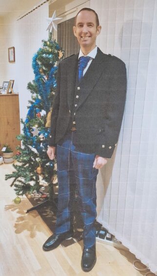 Iain Cotterell in tartan trews standing in front of a Christmas tree.