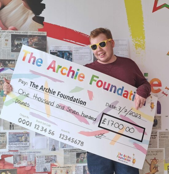 Andrew Batchelor, wearing yellow Sunny Dundee glasses, carries a big cheque for £1,700 made out to the Archie Foundation.