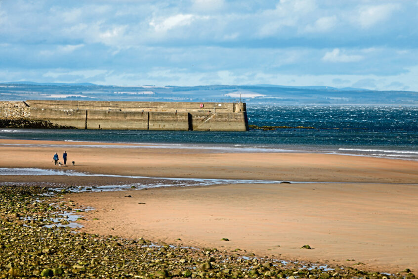 Image show East Sands Beach, St Andrews at low tide. In the foreground is sand and the sea and pier are in the background.