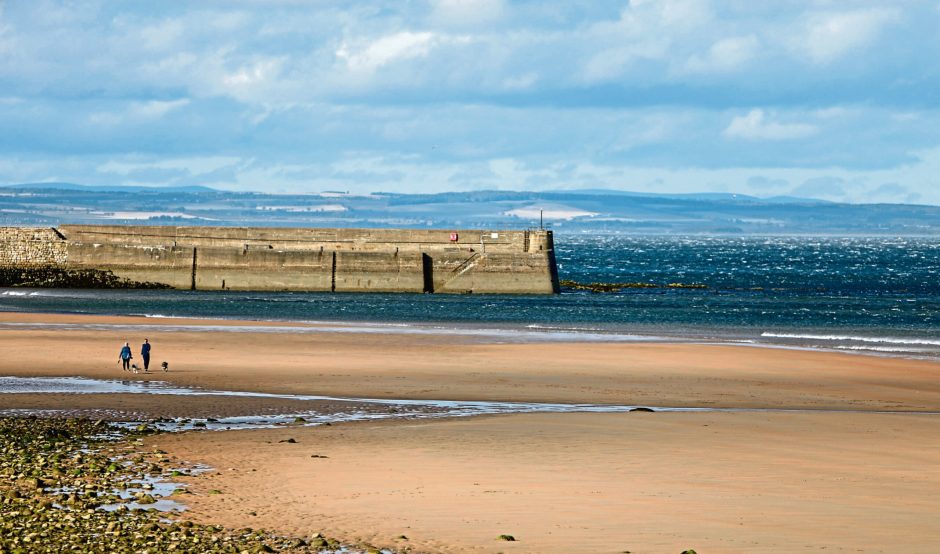 Image show East Sands Beach, St Andrews at low tide. In the foreground is sand and the sea and pier are in the background.