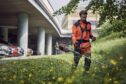 Groundcare professional using brushcutter on grass near a carpark.