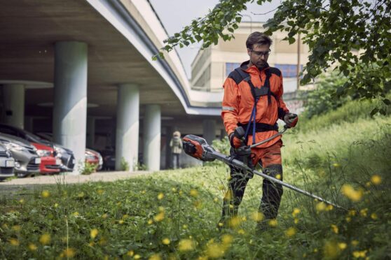 Groundcare professional using brushcutter on grass near a carpark.