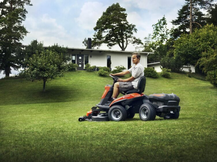 Man cutting large lawn with sit-on mower.