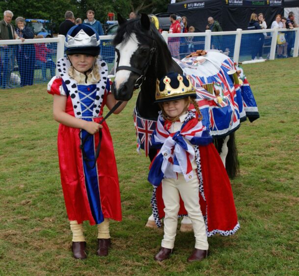 Two small children in union jacks and crowns with a black and white pony draped in union jacks.