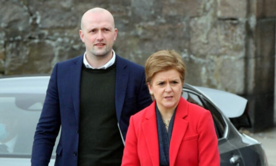 Stephen Flynn in black jumper and dark blue jacket, walking beside former First Minister Nicola Sturgeon, in red blazer, on an SNP campaign visit in Aberdeen.