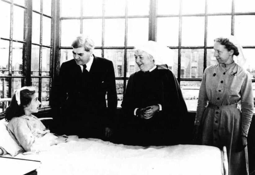 Black and white photo showing NHS founder Aneurin Bevan and two nurses by the hospital bedside of a young girl in 1948.