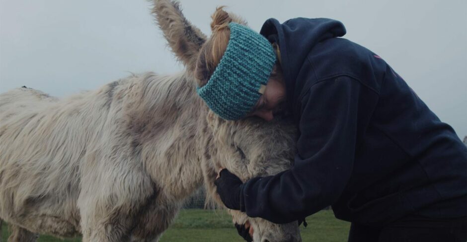 Karen Inkster hugging elderly donkey's head.