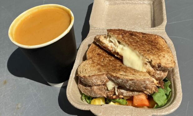 A full cup of soup next to a toastie oozing with melted cheese.