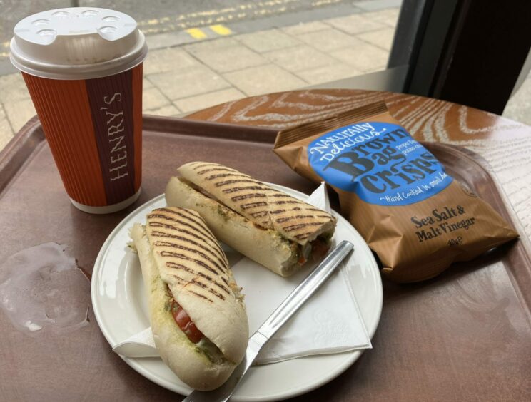 A cafe tray with a takeaway cup, small bag of crisps, and a plate with a mozzarella and pesto panini for Dundee Restaurant Week.