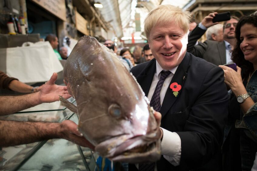 Smiling Boris Johnson on a visit to a street market, holding a large slimy fish.