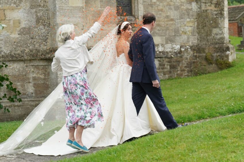 A grey haired woman in a floral dress throws orange confetti over former chancellor George Osborne and his new wife Thea Rogers as they leave church following their wedding.