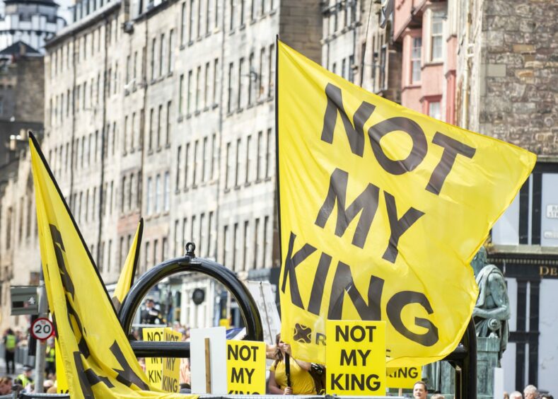 Large yellow and black banners with the slogan 'Not my king' against a background of tenement buildings in the centre of Edinburgh.