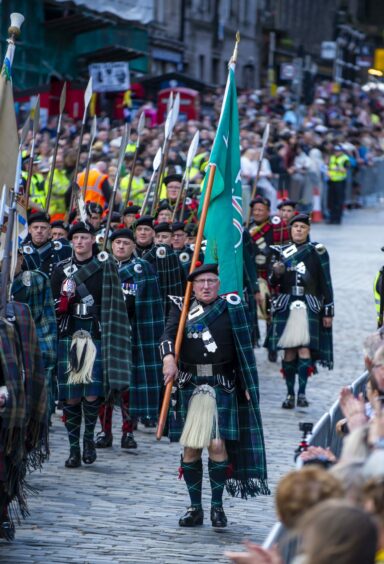 Members of the Royal Company of Archers walk past the crowds on the Royal Mile in full Highland dress.