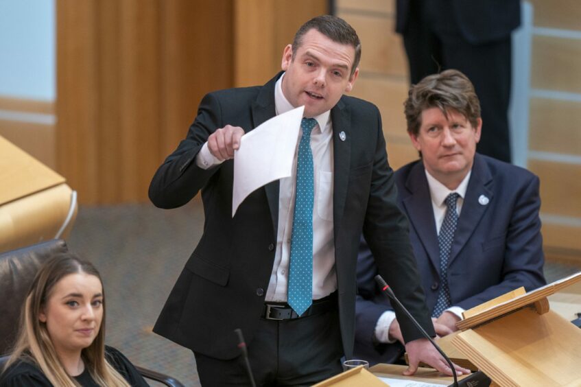 Scottish Conservative leader Douglas Ross waving a paper while addressing the Scottish Parliament, flanked by fellow Conservative MSPs.