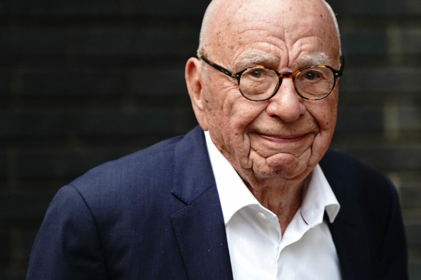 Rupert Murdoch in dark suit jacket and white unbuttoned shirt looking towards photographers as he arrives at a party.