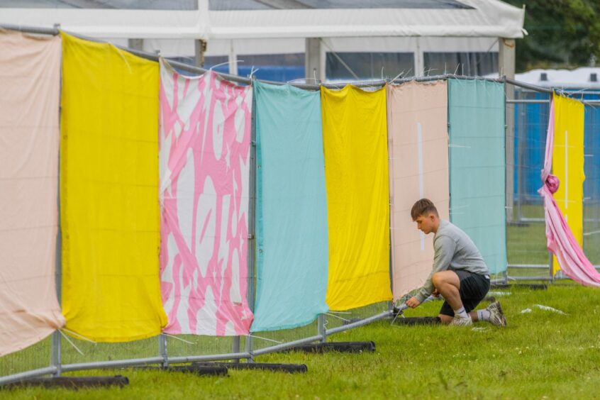 Young man on his knees fixing colourful banners to wire fencing.