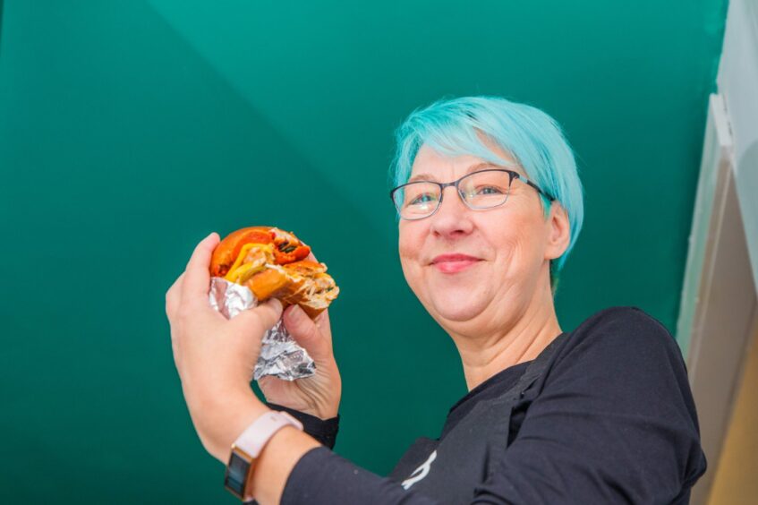 A woman with blue hair holding a Sliderz burger.