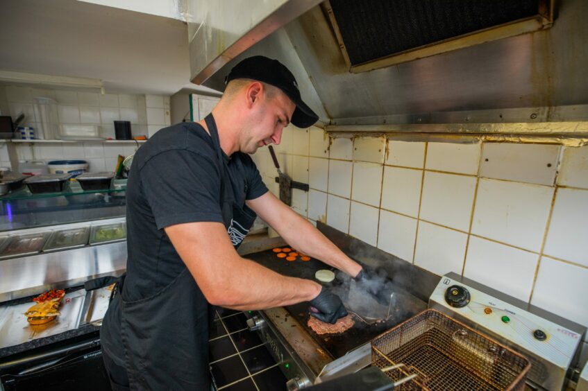 A man in a takeaway kitchen grilling a burger