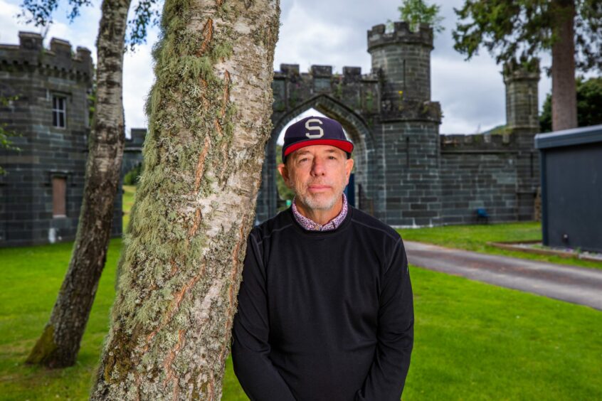 Tom Collopy, Discovery Land Company's chief project officer at Taymouth Castle, leaning against a tree in front of the castle gates.