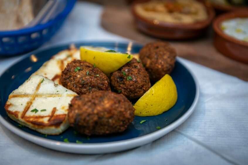 A plate of halloumi and falafel with two slices of lemons.