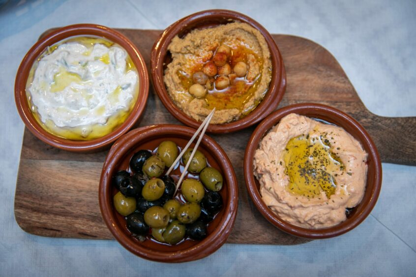 A wooden board with four bowls of dips and olives.