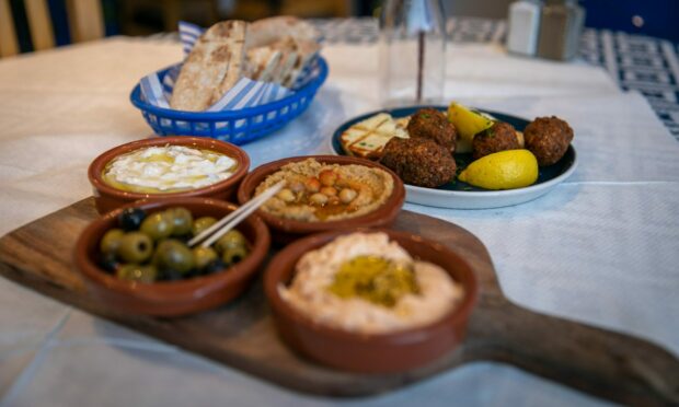 A table at Andreou's Dundee with three different dips, a bowl of olives, a plate of falafel and halloumi, and a basket of pita bread.