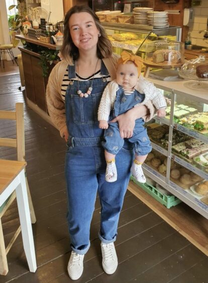 Zoe and six-month old Lily dressed in blue dungarees, white shoes, stripey t-shirts and beige cardigans in Sweetpea Cafe. 
